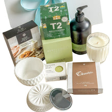 Load image into Gallery viewer, A curated gift box filled with assorted packaged snacks and treats, including a chocolate bar box, chocolate chip cookie, green tea, and a coconut soy candle, body wash, soap  bar, white cannister in a white magnetic gift box
