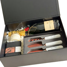 Load image into Gallery viewer, A luxury gift hamper set in a black magnetic gift box, featuring a bottle of Moët &amp; Chandon Imperial Brut, a Meeraboo mini soy hand-poured candle, Cuvee couverture chocolate, and a gift boxed set of cheese knives with white marble handles and copper-colored blades.

