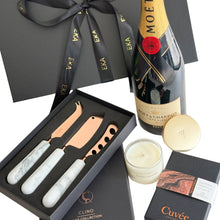 Load image into Gallery viewer, A luxury gift hamper set in a black magnetic gift box, featuring a bottle of Moët &amp; Chandon Imperial Brut, a Meeraboo mini soy hand-poured candle, Cuvee couverture chocolate, and a gift boxed set of cheese knives with white marble handles and copper-colored blades.
