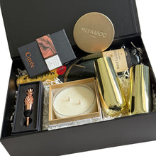 Load image into Gallery viewer, A luxury gift hamper set in an open black magnetic gift box, featuring a round gold-toned Meeraboo hand-poured candle, a pineapple-shaped bottle stopper, a Moet &amp; Chandon  Imperial Brut bottle, and two gold-toned stemless champagne glasses, arranged in white crinkle paper.

