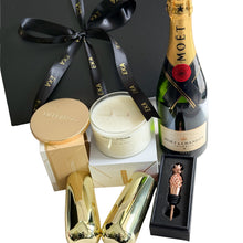 Load image into Gallery viewer, A luxury gift hamper set in an open black magnetic gift box, featuring a round gold-toned Meeraboo hand-poured candle, a pineapple-shaped bottle stopper, a Moet &amp; Chandon  Imperial Brut bottle, and two gold-toned stemless champagne glasses, arranged in white crinkle paper.
