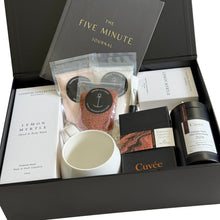 Load image into Gallery viewer, Black magnetic gift box with black five-minute journal, hand-poured candle, Cuvee classic dark hot chocolate, cuvee couverture chocolate, white hug mug, self-care kit and hand and body wash
