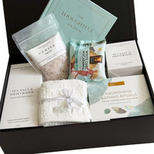 Load image into Gallery viewer, A curated gift set in an open black box featuring a light blue journal, bath salts, a Sheridan face washer in white, boxed sea salt and driftwood candle, a reed diffuser, a bathing rituals soap and bath bomb gift set, and a Byron Bay white choc macadamia cookie
