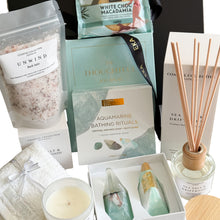 Load image into Gallery viewer, A curated gift set in an open black box featuring a light blue journal, bath salts, a Sheridan face washer in white, boxed sea salt and driftwood candle, a reed diffuser, a bathing rituals soap and bath bomb gift set, and a Byron Bay white choc macadamia cookie
